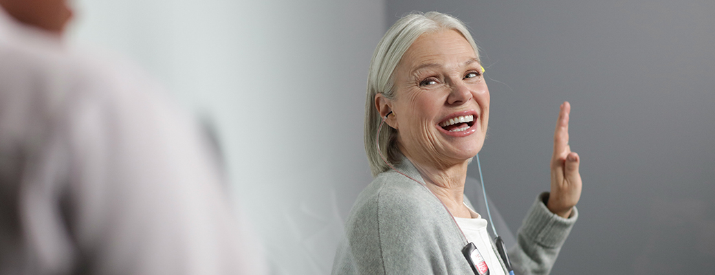 Image of hearing aid patient raising her hand and smiling during a hearing test